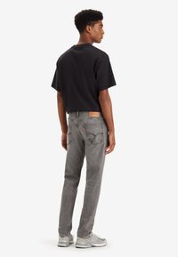 Black cotton T-shirt, relaxed fit, paired with gray denim jeans featuring back pockets and leather patch. Footwear: gray sneakers.