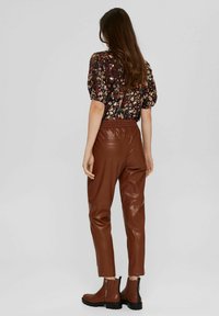 Bruine neplederen broek met een elastische taille, gecombineerd met een blouse met bloemenprint. De outfit wordt compleet gemaakt met bruine enkellaarzen.