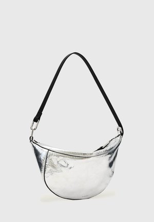 Bolso de hombro metálico plateado con forma de media luna, con correa negra ajustable y cierre de cremallera sobre fondo liso claro.