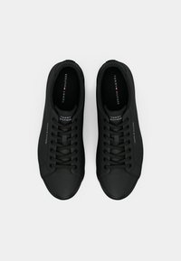 Fekete Tommy Hilfiger sneaker pár fűzőkkel, logóval a nyelvén, oldalán és talpbetéteken, felülnézetből, fehér háttér előtt.