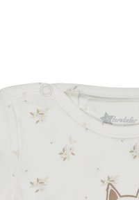 White cotton baby onesie with small beige floral pattern, round neckline, and snap button closure. Features a fox graphic on the front.