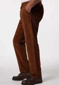 Pantalones de pana marrones con un ajuste relajado, que presentan bolsillos laterales y un cordón en la cintura, mostrados de lado.