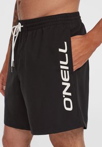 Fekete úszónadrág, zsinóros derékrésszel és oldalsó zsebekkel. Feltűnő fehér "O'NEILL" logóval, amely függőlegesen van nyomtatva az oldalon.