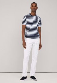 Marynarska niebiesko-biała koszulka z krótkim rękawem, zestawiona z białymi dżinsami i niebieskimi sneakersami. Gładka bawełniana tkanina, klasyczny fason z okrągłym dekoltem.