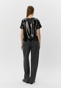 Sort pailletetop med korte ærmer, der har en rund halsudskæring og en knapdetalje bagpå. Sammen med grå leopardprint brede bukser.