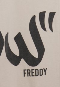 Tela beige con un gran diseño gráfico negro que presenta letras estilizadas que dicen "Freddy". La textura parece suave y plana.