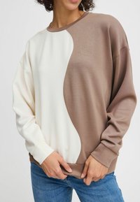 Sweatshirt marron et crème avec un design en couleurs bloc courbé, des manches longues, des poignets côtelés et un col rond. Texture de tissu lisse.