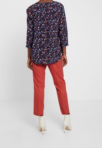 Marinblomstrad blus med trekvartsärmar, i kombination med korallfärgade byxor. Blusen har en rund halsringning och en lös passform.