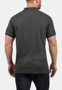 Mørkegrå kortærmet polo-shirt med krave, der har et mærke på venstre ærme, glat stof og en lige kant.