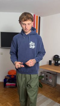 Tamsiai mėlynas su kapuci megztinis su grafine spauda ant krūtinės, derinamas su laisvomis alyvuogių žalios spalvos krovinių kelnėmis. Medžiaga atrodo minkšta ir kasdieniška.