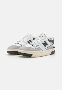 White and gray athletic shoes with suede detailing, textured rubber sole, black accents, and prominent "N" logo on the side.