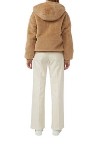 Tan faux fur gewatteerde jas met een relaxte pasvorm, geribbelde boorden en een beige binnenkant, gecombineerd met brede crèmekleurige broeken en witte sneakers.