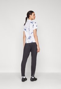 Kortermet skjorte i hvitt med blå abstrakte mønstre, kombinert med svarte tapered bukser og svarte joggesko; glatte teksturer og slank passform.