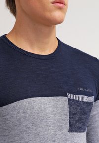 Marineblaue und graue, farbblockierte Strickjacke. Verfügt über einen Rundhalsausschnitt, strukturierte Stoffqualität und eine Brusttasche mit gestreiftem Besatz und dekorativen Nähten.