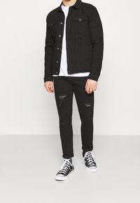 Svart denimjacka med knap stängning och bröstfickor, matchad med svarta slitna jeans och svarta högskoor. Oprydd vit t-shirt.