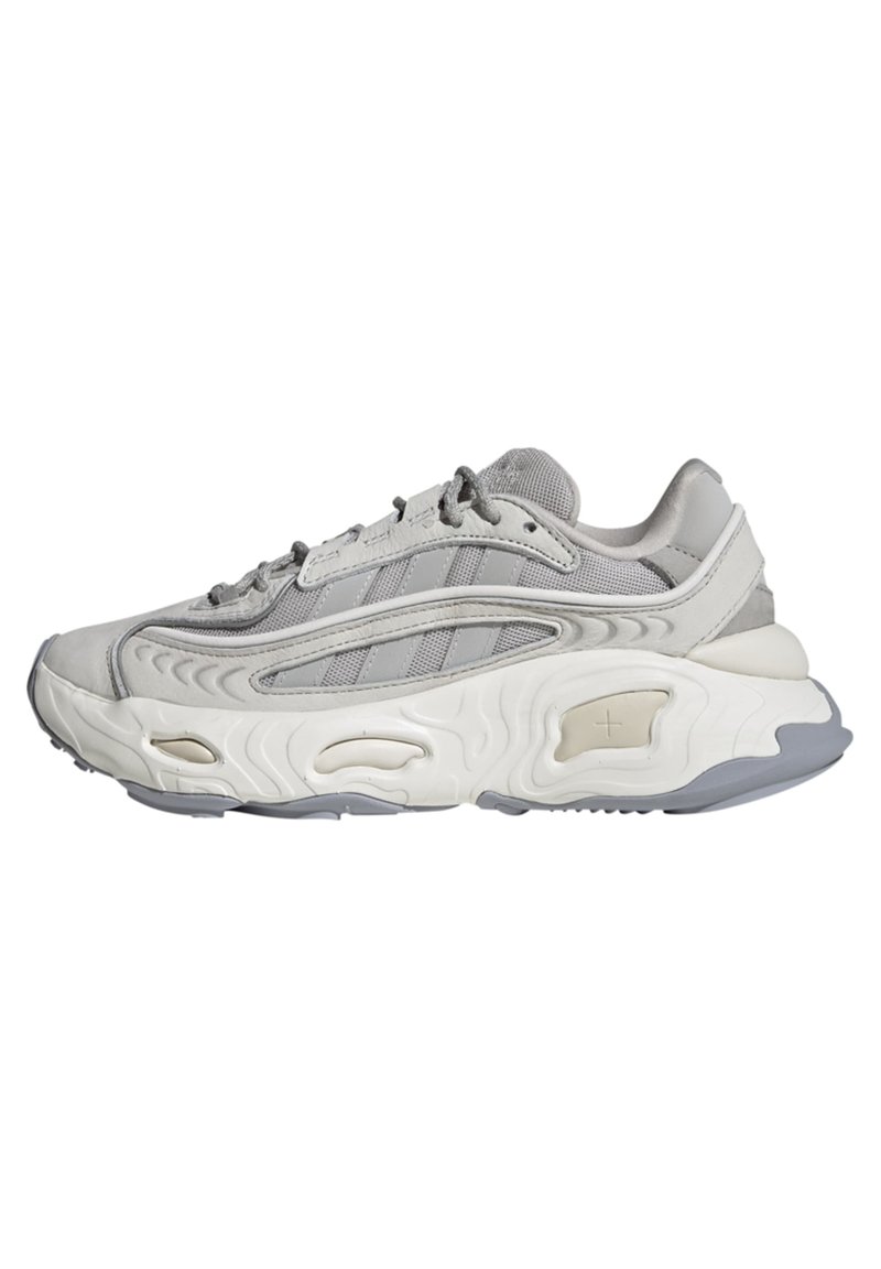 Graue Sportschuhe mit einem glatten, strukturierten Obermaterial, das Netzpaneele und drei tonal angepasste Streifen aufweist. Dicke weiße Sohle mit Ausschnitten und grauen Akzenten.