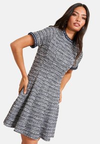 Rövid ujjú, testhez simuló és szoknyában bővülő fazonú ruha texturált anyagból, tengerészkék és fehér színben, kerek nyakkivágással és kontrasztos peremmel az ujjain.