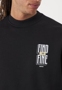 Svart hettegenser med ribbet krage og trykt grafikk som har ordene "FIND ALLA FINE" i fet hvit og gul tekst, merket med "Juventus."
