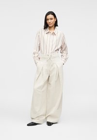 Vaaleat, leveälahkeiset housut, joissa on nyörivöinti vyötäröllä ja laskokset, yhdistetty pehmeissä pastellisävyissä olevaan raidalliseen nappipaitaan.