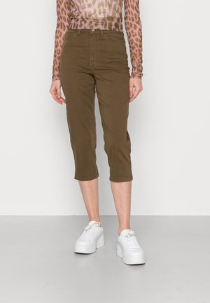 Calças cropped verdes oliva em twill de algodão com uma cintura alta, apresentando bolsos laterais e corte straight leg, combinadas com sapatilhas brancas de plataforma.