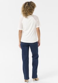 T-shirt blanc à manches courtes avec des manches en maille texturée, associé à un jean en denim bleu foncé et des chaussures à talons marron clair.