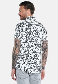 Kurzarmpoloshirt in Weiß mit einem geometrischen schwarzen Linienmuster, das über einen Kragen und eine lockere Passform verfügt.