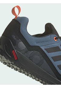 Niebieskie i czarne buty sportowe z teksturowaną cholewką, czarną gumową podeszwą, czerwonym akcentem na pięcie oraz subtelnymi detalami graficznymi po boku.