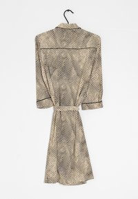 Långärmad klänning i knälängd med ett beige och svart geometriskt mönster. Har en krage, ett bälte i midjan och knapppdetaljer vid ärmsluten.