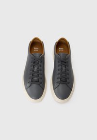 Grå lærersneakers med en glat tekstur, rund tå, kontrasterende beige gummisål og mørkegrå snørebånd. Mærkelogo synlig indeni.