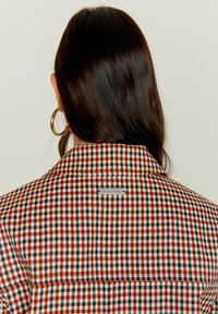 Ruuduline särk, millel on punane, must ja valge muster, kraega kaelus ja taga metallタグ, millel on kiri "House of Sunny".