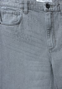 Jeans in denim grigio con tasca frontale e dettagli strappati vicino alla vita. Il materiale è morbido con una sottile trama e una finitura liscia.