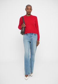 Červený, priliehavý sveter s gombíkmi vpredu; skombinovaný so svetlo modrými rozšírenými džínsami a bielymi lodičkami s špicatým nosom; čierna crossbody taška.