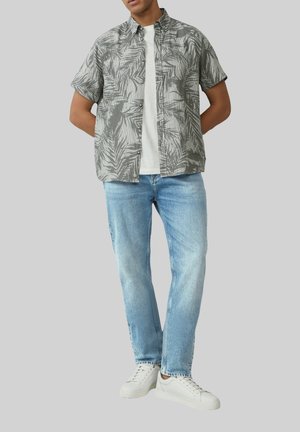 Kurzärmliges graues Hemd mit Palmenblattmuster, über einem weißen T-Shirt, kombiniert mit hellblauen Jeans und weißen Turnschuhen.
