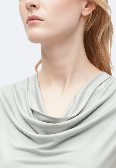 Top grigio chiaro con scollatura drappeggiata, realizzato in tessuto morbido. La texture appare liscia e leggermente elasticizzata. Nessun motivo visibile o hardware.