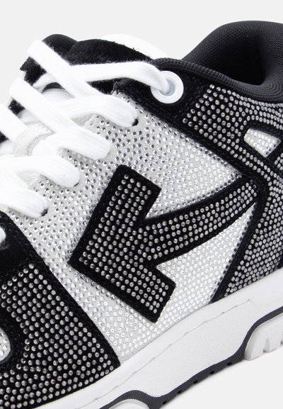 Λευκό και μαύρο αθλητικό παπούτσι με επάνω μέρος διακοσμημένο με στρας και μαύρες σουέτ λεπτομέρειες, με λευκά κορδόνια και λευκή λαστιχένια σόλα.