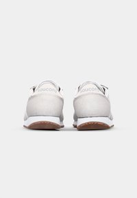 Tenisky Saucony s vrškem z lehké šedé semiše, bílými akcenty a hnědým texturovaným gumovým podrážkou. Na patě je minimální označení značky.