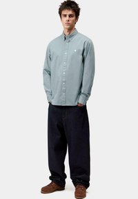 Camisa de botones de manga larga de color azul claro con cuello, combinada con pantalones holgados de mezclilla oscura y zapatos marrones. Diseño sencillo, sin patrones.