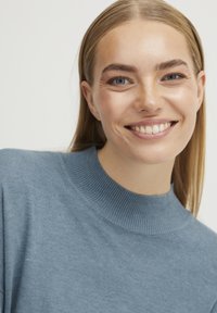 Pull bleu clair avec un col côtelé et une texture douce, offrant une coupe décontractée. Le matériau paraît lisse avec des variations subtiles.
