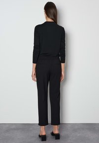 Zwart langarm T-shirt met ronde hals, gecombineerd met zwarte, elastische broek met een tailleband en blokhakken sandalen, gezien van achteren.