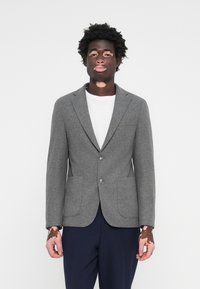 Grå ullblazer med spetsig krage, två framfickor och två knappar. Kombinerad med en vit t-shirt och mörka byxor.