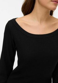 Černý žebrovaný pletený svetr se širokým kulatým výstřihem. Má dlouhé rukávy a přiléhavý střih. Měkká textura, vhodná pro vrstvení.