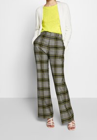 Pantalons à carreaux gris avec des lignes jaunes, taille haute, coupe large. Associés à un haut jaune vif et des sandales blanches à lanières.