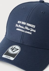 Μπλε σκουφί του μπέιζμπολ με άσπρο κεντητό κείμενο "New York Yankees The Bronx, New York, American League" και μαύρη-λευκή ετικέτα με την ένδειξη "'47 OSFA".