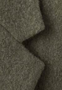 Fieltro de lana en un verde oliva apagado, con una textura suave y borrosa, con fibras visibles, dispuestas en una disposición plegada.