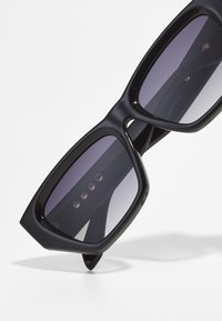 Black sunglasses with a geometric cat-eye shape, gradient lenses, and three decorative rivets on each temple. Smooth, glossy texture.