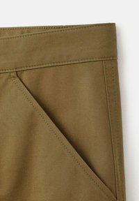 Primer plano de un bolsillo de tela marrón con costuras visibles en una prenda, destacando detalles de la cintura y el borde del bolsillo.