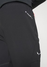 Black outdoor pants made from durable fabric, featuring a zippered pocket, subtle branding, and a sleek, streamlined design.