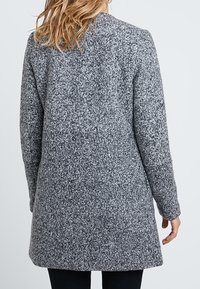 Szary, teksturowany płaszcz z długimi rękawami, o długości do połowy uda i prostym kroju. Charakteryzuje się prostym dekoltem oraz brakiem widocznych zapięć.