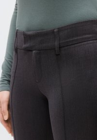 Μαύροι ελαστικοί παντελόνες με ψηλή μέση και ομαλή υφή, με εμπρόσθιες τσέπες και κρυφό φερμουάρ, παρουσιασμένοι μαζί με γκρι μπλούζα μακρυμάνικη.