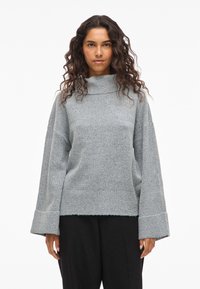 Helles graues, übergroßes Sweatshirt mit hohem Kragen, weiten Ärmeln und rohem Saum, aus einem weichen Strickmaterial hergestellt.